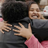 A young woman embraces her neighbor